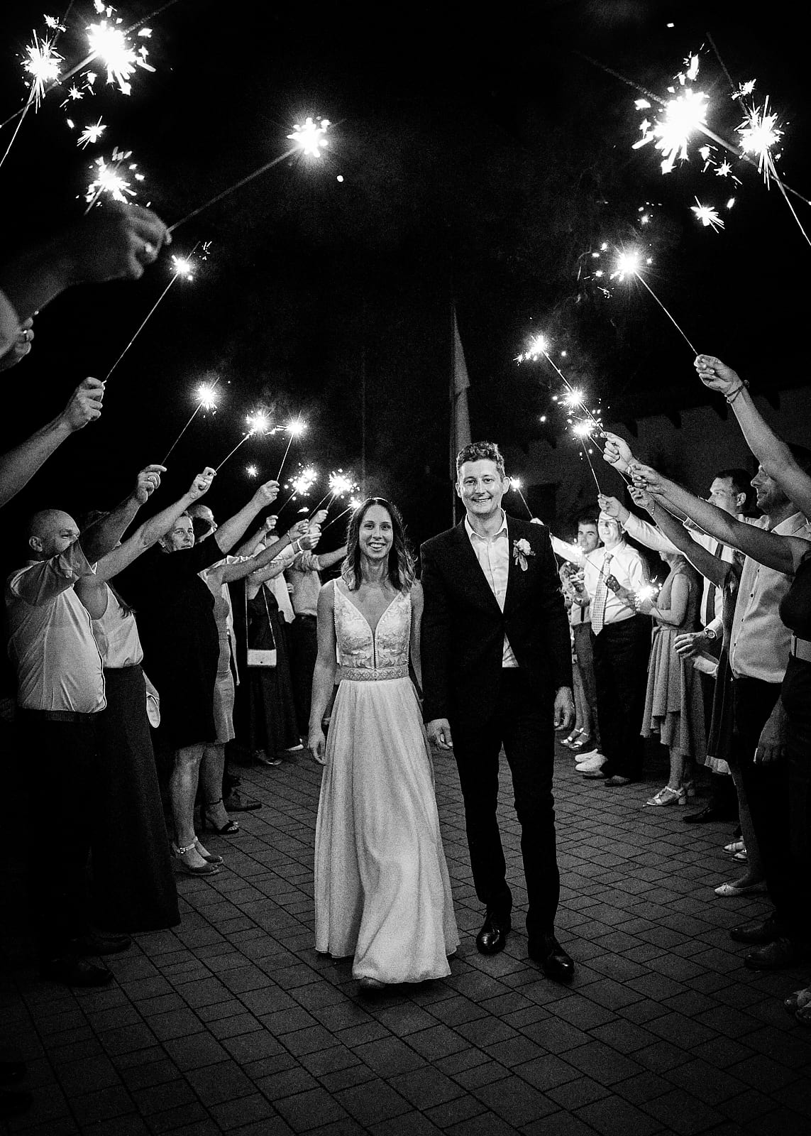 Orsi és Attila kézenfogva sétálnak, miközben csillagszórós sorfalat áll nekik a násznép