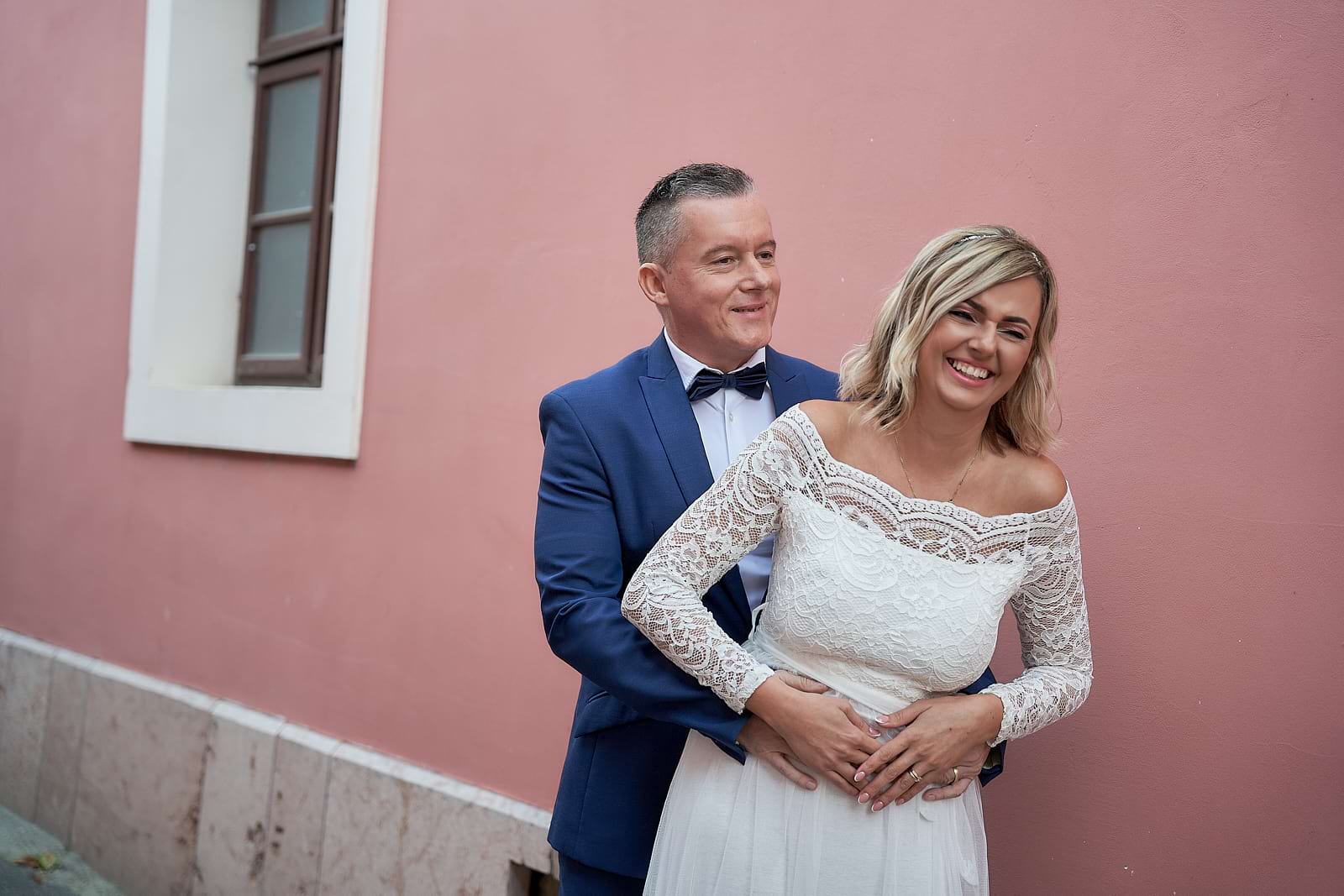 Timi és Miki rózsaszínű fal előtt ölelik meg egymást